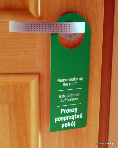 Zawieszka hotelowa na drzwi strona z białym napisem Proszę posprzątać pokój na zielonym tle.